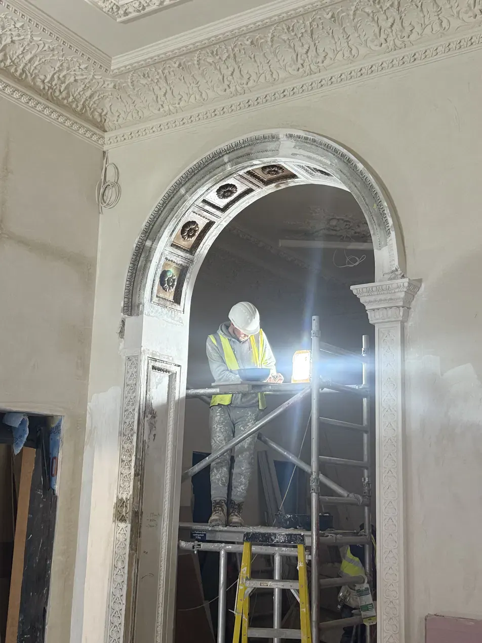 Plasterer working on ornate plaster archway from scaffold