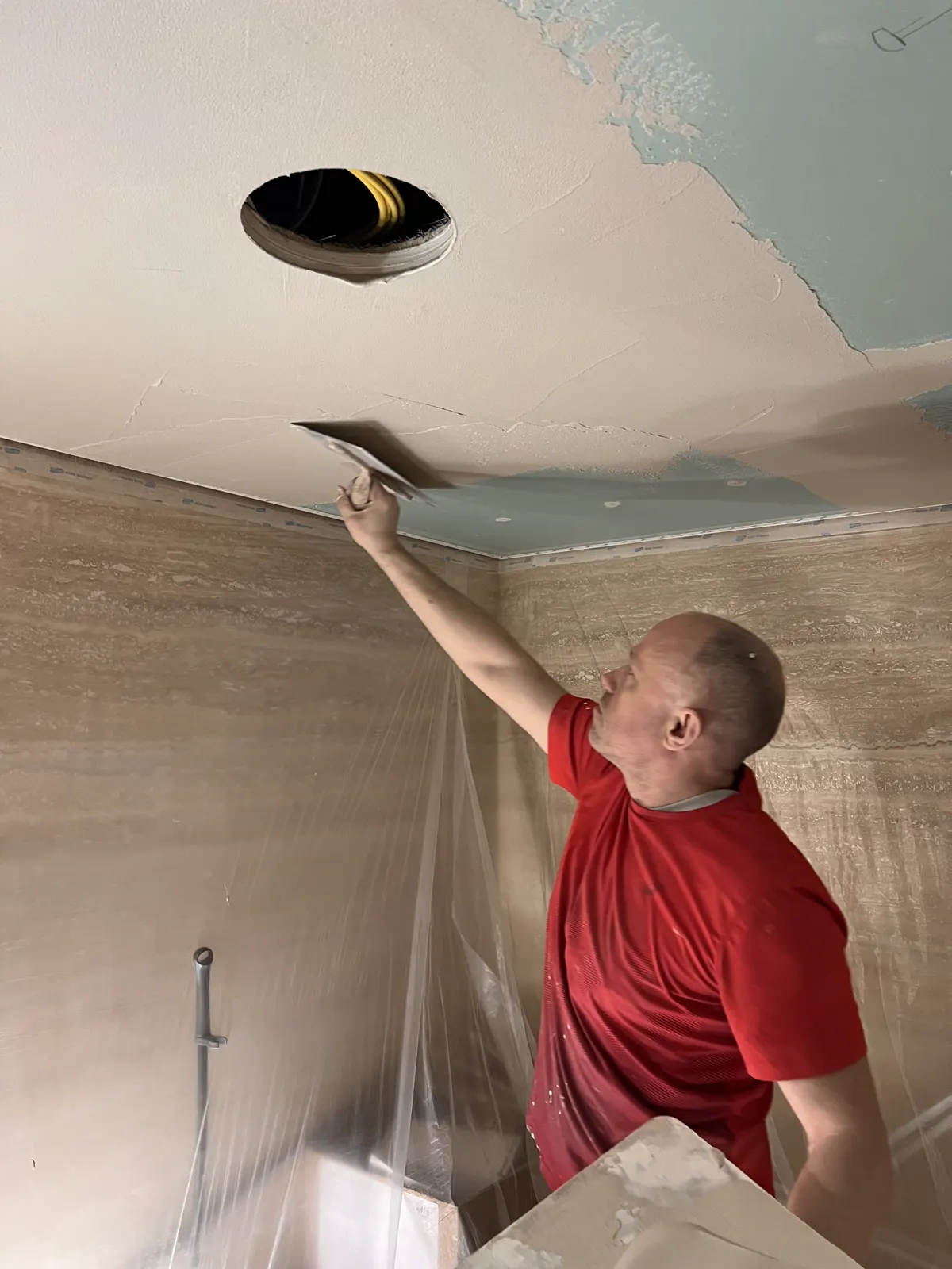 Plasterer skimming a ceiling around a recessed light on a London project