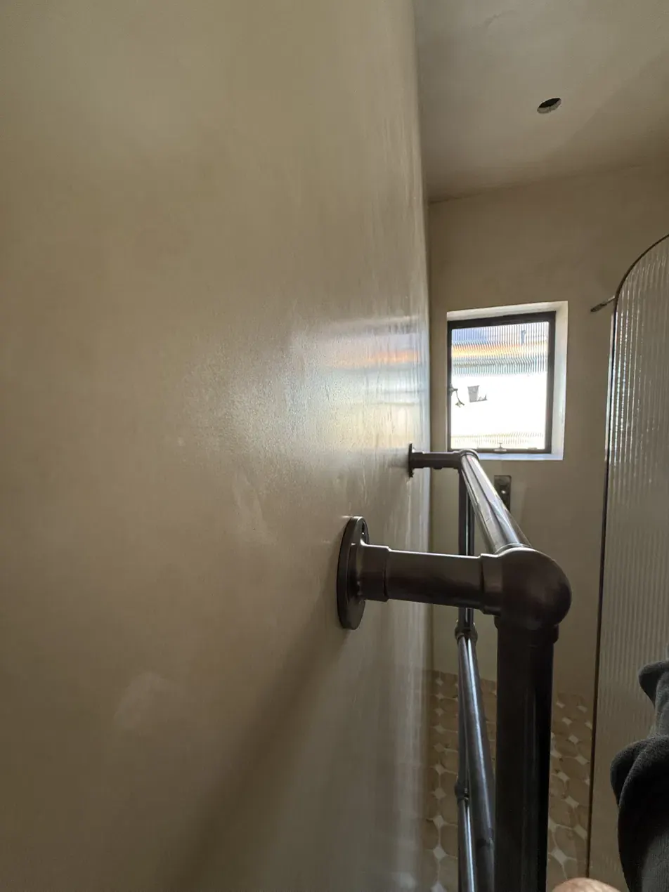 Polished tadelakt wall in a London wet room, raking light showing the surface sheen
