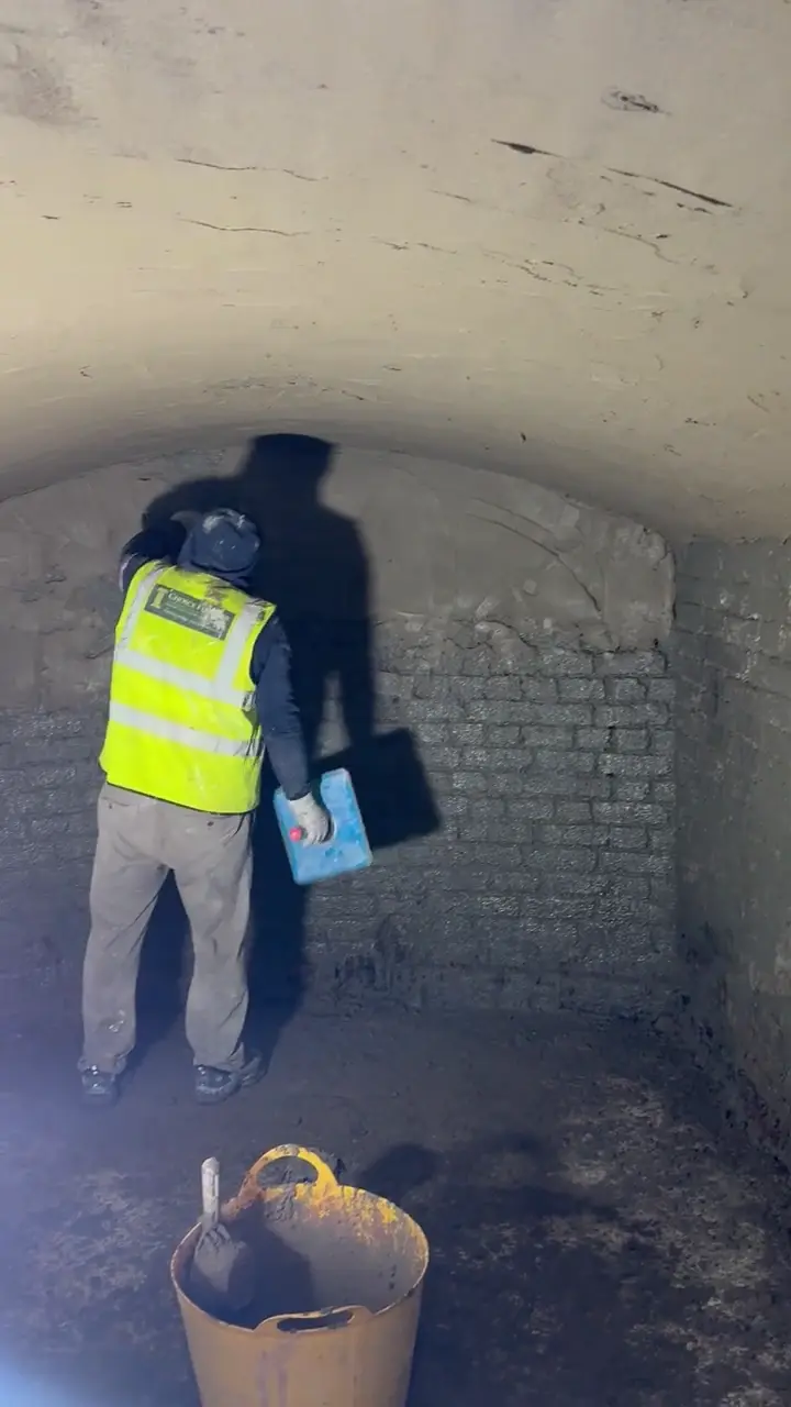 Worker applying a coating to masonry inside an arched basement