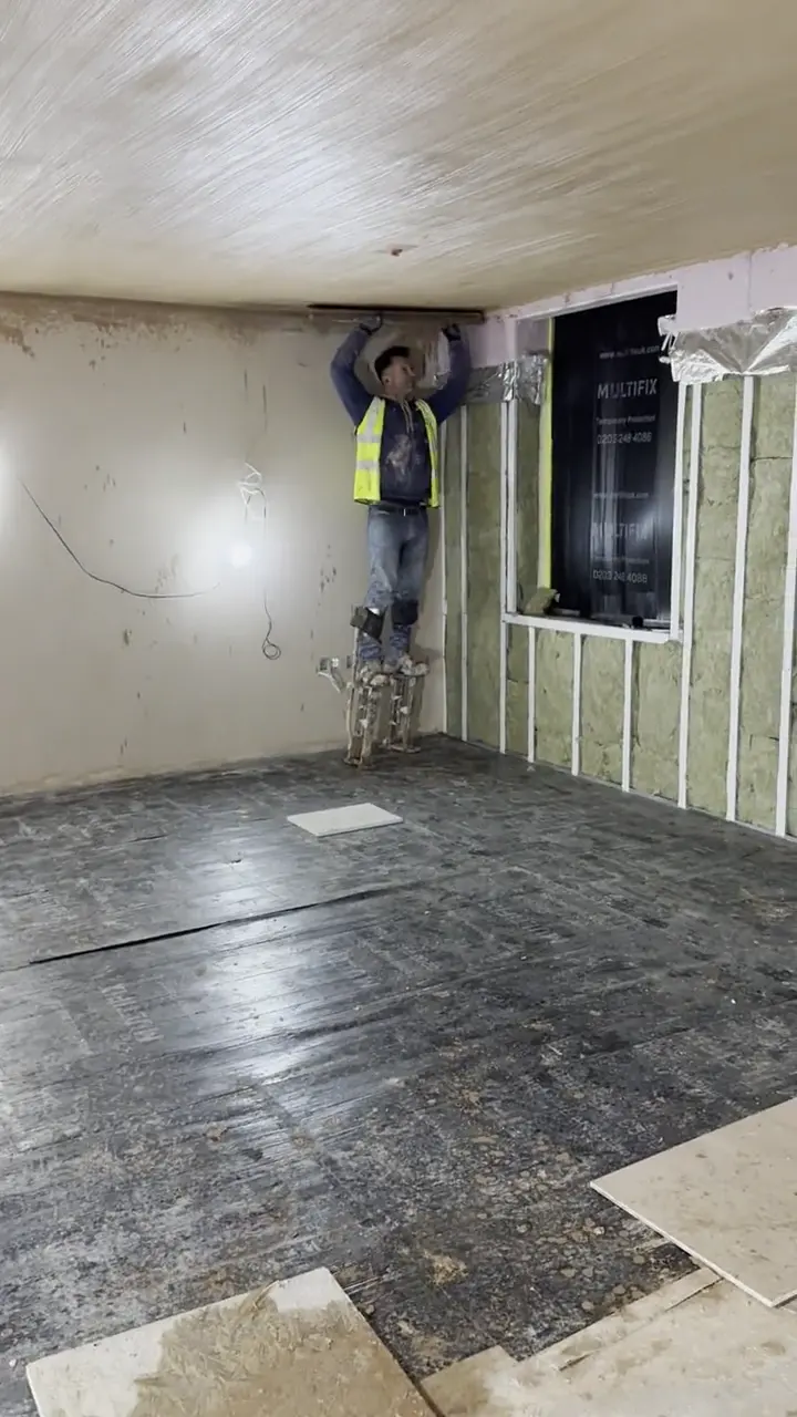 Plasterer on stilts working a ceiling edge, London